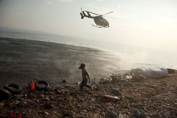 Vrtulník evropské agentury Frontex přelétá u syrského chlapce, který se právě vylodil na řeckém ostrově Lesbos. Tam běženci momentálně tvoří zhruba pětinu lidí.