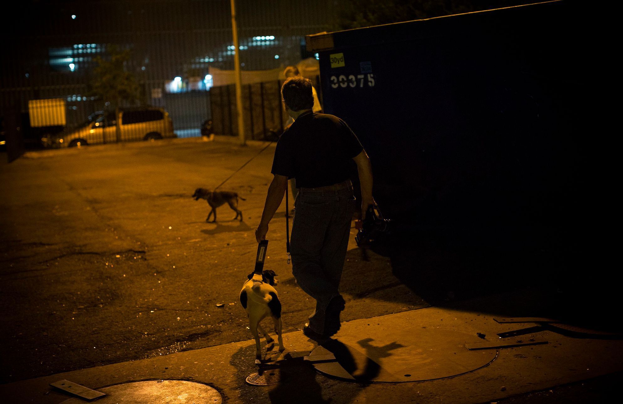 Bill leads his dog Paco, a Feist Terrier, though a vacant lot near trash dumpsters during an organized rat hunt on New York City's Lower East Side
