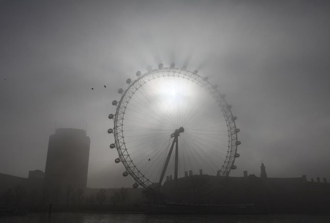 Slunce se prokousává skrze mlhu Londýna. Ráno u turistické atrakce London Eye.