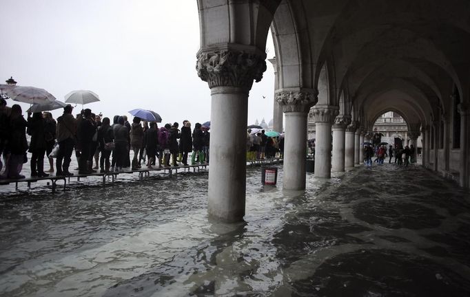 Tourists walk on raised platforms for flood waters in St. Mark Square during a period of seasonal high water in Venice October 27, 2012. The water level in the canal city rose to 127 cm (50 inches) above the normal level, according to the monitoring institute. REUTERS/Manuel Silvestri (ITALY - Tags: ENVIRONMENT SOCIETY TRAVEL) Published: Říj. 27, 2012, 12:12 odp.