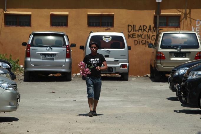 An Australian relative of a victim from the 2002 Bali bombings holds flowers as he walks out of the carpark at Sari Club, which was one of the bombing sites, ahead of the 10th anniversary in Kuta, on the resort island of Bali October 10, 2012. Eighty-eight Australians were among the 202 people killed in the attacks on Sari Club and Paddy's Bar at the popular tourist area of Kuta on October 12, 2002. The graffiti in the background reads, "It is prohibited to urinate here." REUTERS/Beawiharta (INDONESIA - Tags: ANNIVERSARY SOCIETY) Published: Říj. 10, 2012, 5:34 dop.