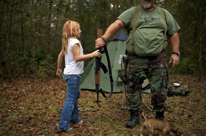 Brianna, 9, of the North Florida Survival Group hands an AK-47 rifle to Jim Foster, 57, the group's leader, before heading out to conduct enemy contact drills during a field training exercise in Old Town, Florida, December 8, 2012. The group trains children and adults alike to handle weapons and survive in the wild. The group passionately supports the right of U.S. citizens to bear arms and its website states that it aims to teach "patriots to survive in order to protect and defend our Constitution against all enemy threats". Picture taken December 8, 2013. REUTERS/Brian Blanco (UNITED STATES - Tags: SOCIETY POLITICS TPX IMAGES OF THE DAY) ATTENTION EDITORS: PICTURE 2 20 FOR PACKAGE 'TRAINING CHILD SURVIVALISTS' SEARCH 'FLORIDA SURVIVAL' FOR ALL Published: Úno. 22, 2013, 1:06 odp.