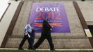 Pedestrians walk past a large debate sign hanging from a building during preparations for Tuesday's U.S. presidential debate at Hofstra University in Hempstead, New York, October 15, 2012. REUTERS/Lucas Jackson (UNITED STATES - Tags: POLITICS USA PRESIDENTIAL ELECTION ELECTIONS) Published: Říj. 15, 2012, 11:20 odp.