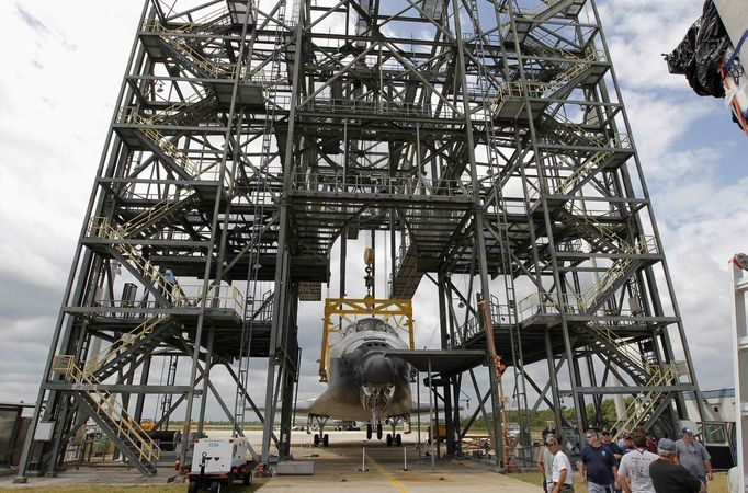 Space center workers stand near the space shuttle Discovery after it was attached to a lifting harness in the Mate Demate facility at Kennedy Space Center in Cape Canaveral