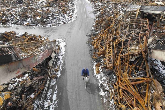 Cyklista jednoucí mezi zničenými domy ve městě Kesennuma.