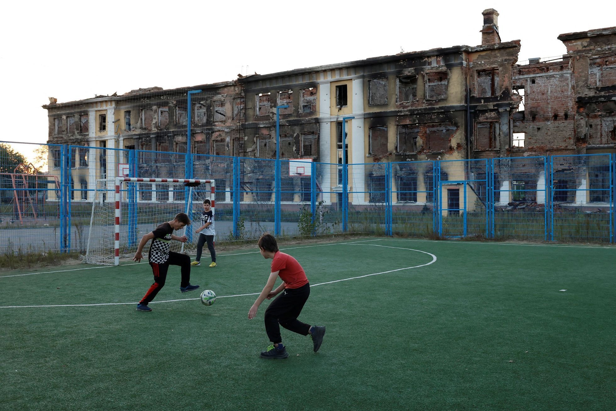 Školáci hrají fotbal před vybombardovanou budovou školy v Charkově.