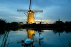 Pár labutí plave v popředí osvětleného vodního mlýna za soumraku v Kinderdijku, Holandsku, 6. září 2003. Kinderdijk, známý svojí sbírkou funkčních vodních mlýnů, osvětluje všechny mlýny, aby oznámil konec turistické sezóny.