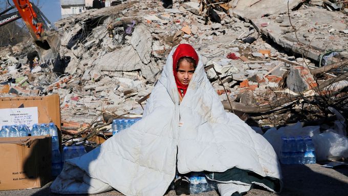 Dívka sedí poblíž místa zřícené budovy po zemětřesení v tureckém Kahramanmarasu.