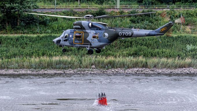 Nasazený armádní vrtulník nabírá vodu z Labe.
