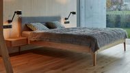 Jednoduchému prostoru dominuje světlé dřevo a postel s čalouněním.
