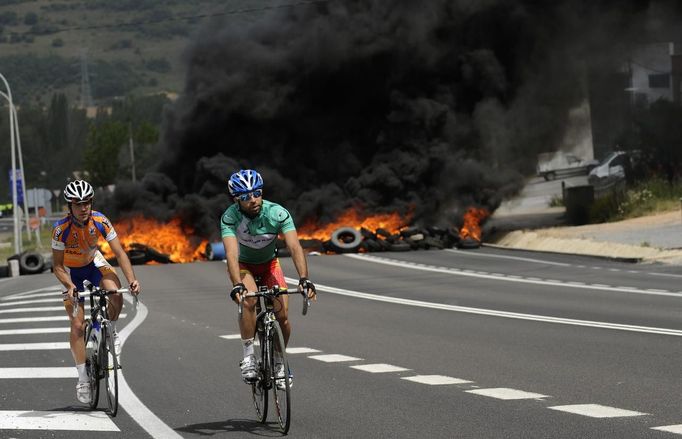 Riders pedal on the N-630 road past a fire barricade set up by miners in La Robla, near Leon, northern Spain June 20, 2012. The miners were protesting against the government's proposal to decrease funding for coal production. REUTERS/Eloy Alonso (SPAIN - Tags: CIVIL UNREST POLITICS BUSINESS EMPLOYMENT SPORT CYCLING) Published: Čer. 20, 2012, 1:02 odp.