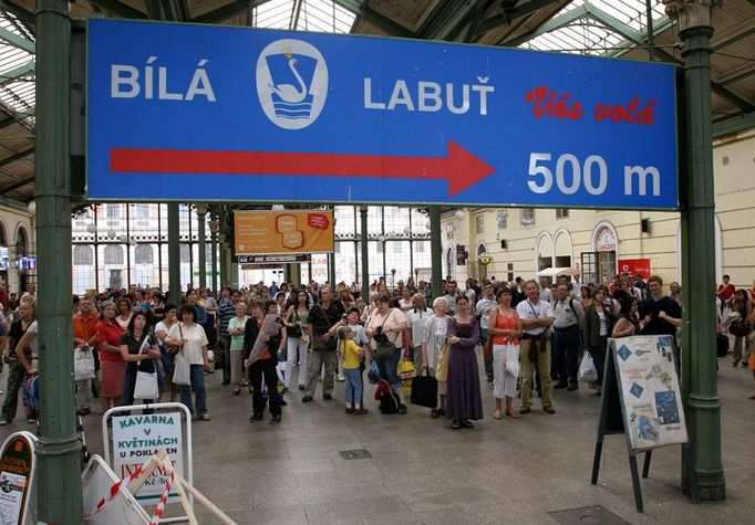 Pohled z druhé strany. Hlouček čekajících před tabulí s odjezdy vlaků roste. Laviček je v hale jen několik, čekárna žádná.