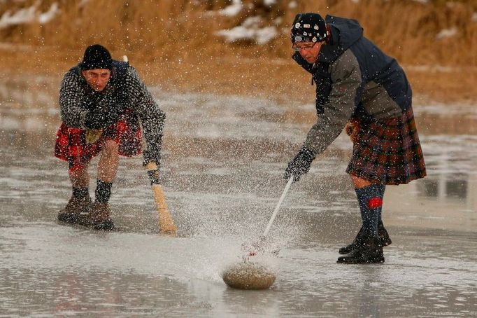 Curling na skotský způsob. Kenny Kinnear (vlevo) a David Smith hrají na zamrzlém jezeře Menteith v hrabství Stirlingshire. V Británii už se oteplilo, led pomalu odtává, proto ty gejzíry vody.