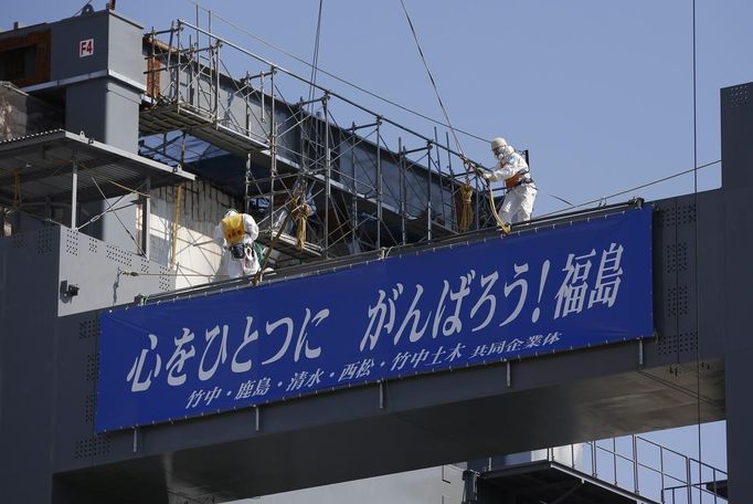 Workers wearing protective suits and masks are seen on top of a foundation construction for the storage of melted fuel rods, next to the No.4 reactor at Tokyo Electric Power Company's (TEPCO) tsunami-crippled Fukushima Daiichi nuclear power plant in Fukushima prefecture March 6, 2013, ahead of the second-year of anniversary of the the March 11, 2011 tsunami and earthquake. The banner reads: "Unite the Heart, Gambaro! Fukushima (Go! Fukushima)". REUTERS/Issei Kato (JAPAN - Tags: DISASTER ANNIVERSARY) Published: Bře. 6, 2013, 10:31 dop.