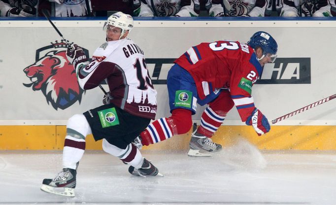 Hokejista Guntis Galvinš vyhazuje před Ľubošem Bartečkem v utkání KHL 2012/13 mezi Lvem Praha s Dinamem Riga.