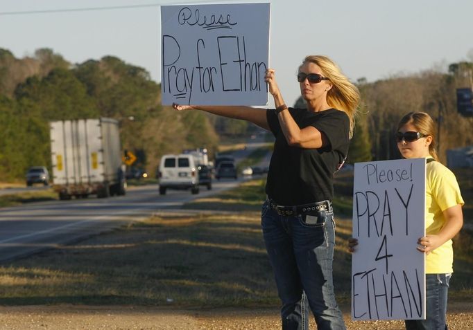 Sherry Johnson Parker and her daughter Olivia Parker hold signs along Highway 231 asking drivers to pray for Ethan, a 5-year-old boy taken hostage five days ago, after a bus driver was shot and killed near Midland City, Alabama February 3, 2013. Mourners in the small town of Midland City, Alabama, gathered on Sunday to bury a school bus driver slain during the abduction of a child taken captive and held for a sixth day by a gunman in an underground bunker. REUTERS/Phil Sears (UNITED STATES - Tags: CRIME LAW OBITUARY) Published: Úno. 4, 2013, 1:20 dop.