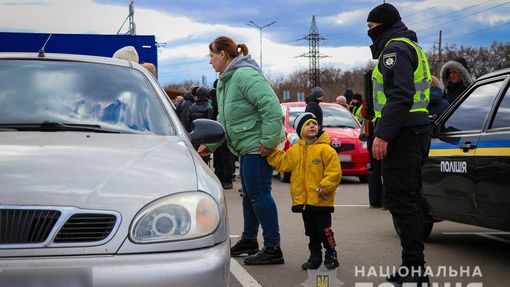 Lidé prchající z Mariupolu stojí vedle ukrajinského policisty.