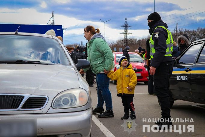 Lidé prchající z Mariupolu stojí vedle ukrajinského policisty.