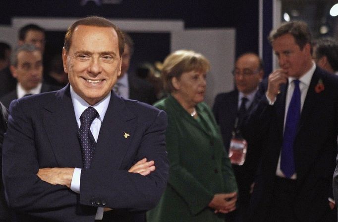 Berlusconi pózuje před fotoaparáty, zatímco německá kancléřka Angela Merkelová se v pozadí baví s britským premiérem Davidem Cameronem na summitu zemí skupiny G20 v Cannes - 3. listopadu 2011.