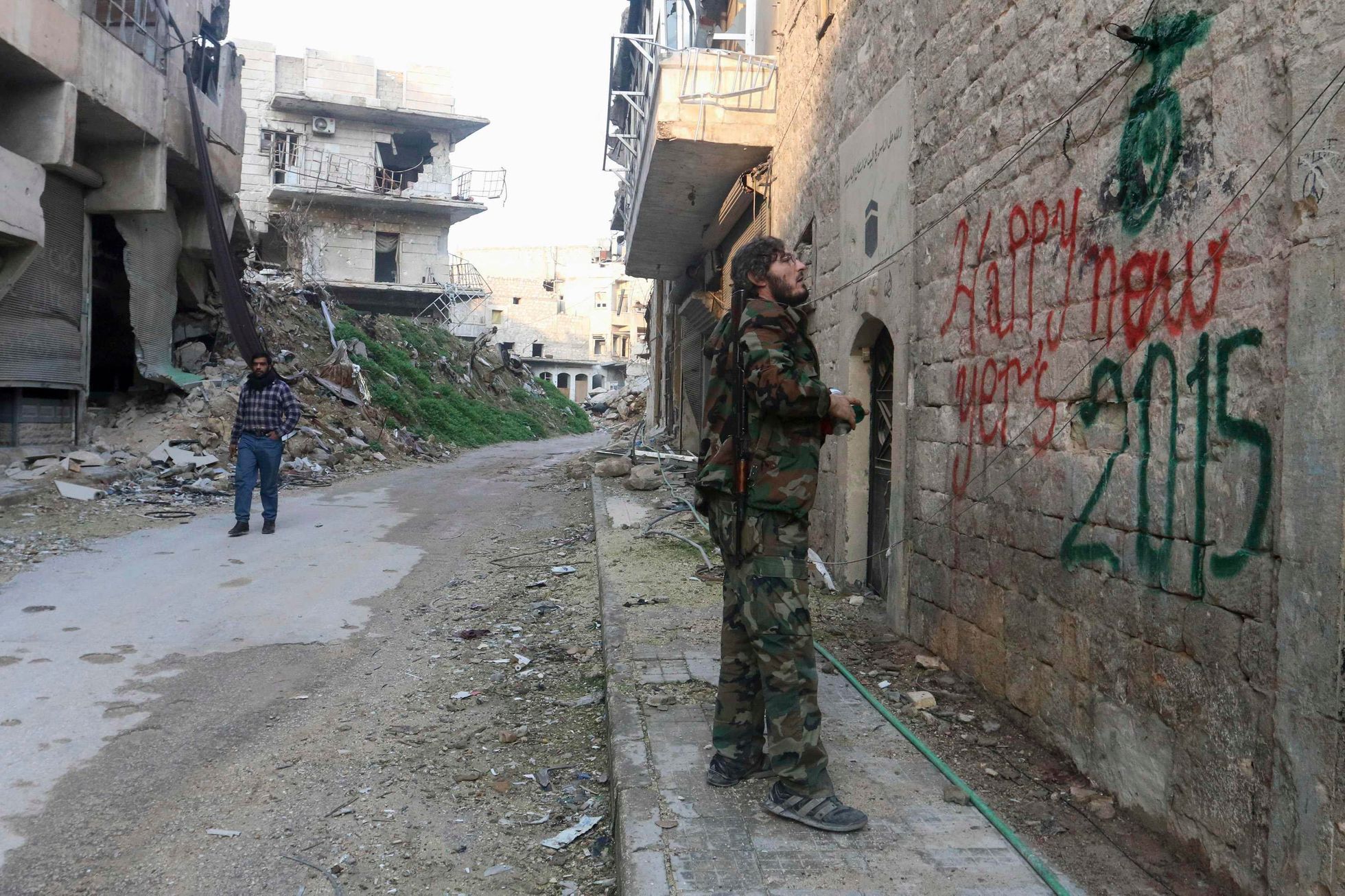 A Free Syrian Army fighter sprays graffiti on a wall prior to the new year in Aleppo
