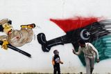 Muž si hraje se synem na ulici ve městě Benghází před graffiti, které znázorňuje Muammara Kaddáfího.