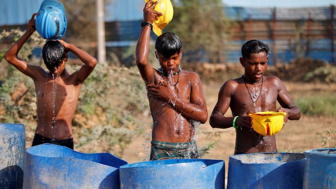 Pracovníci v Ahmedabadu se osvěžují v horkých dnech pomocí svých helem vodou z přilehlých barelů.