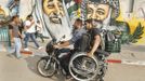 Wheelchair-bound Palestinian freelance photographer Moamen Qreiqea holds his wheelchair as he rides on a motorcycle past murals of late leader Yasser Arafat (R) and late Hamas spiritual leader Ahmed Yassin, on a street in Gaza City October 1, 2012. Qreiqea, 25, lost both his legs in an Israeli air strike in 2008 while taking pictures east of Gaza. The father of two is determined to continue his career despite his disability. REUTERS/Suhaib Salem (GAZA - Tags: SOCIETY MEDIA) Published: Říj. 1, 2012, 3:39 odp.