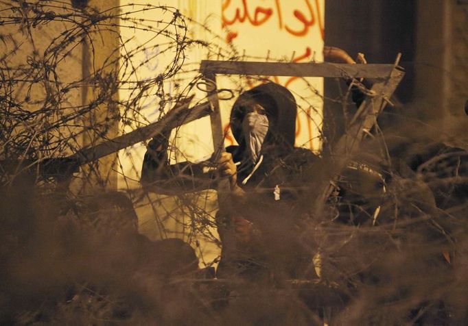 A masked protester opposing Egyptian President Mohamed Mursi and the Muslim Brotherhood, tries to cut through barbed wires to break through one of the gates of the Presidential Palace, in Cairo February 11, 2013. Protesters demanding the departure of Mursi clashed with police outside his palace on Monday on the second anniversary of the overthrow of veteran autocrat Hosni Mubarak. Dozens of youths threw rocks at the Ettihadiya palace after a peaceful march by thousands of demonstrators who accused Mursi's conservative Muslim Brotherhood of hijacking Egypt's democratic revolution and seeking to monopolise power. REUTERS/Asmaa Waguih (EGYPT - Tags: POLITICS CIVIL UNREST) Published: Úno. 11, 2013, 7:37 odp.