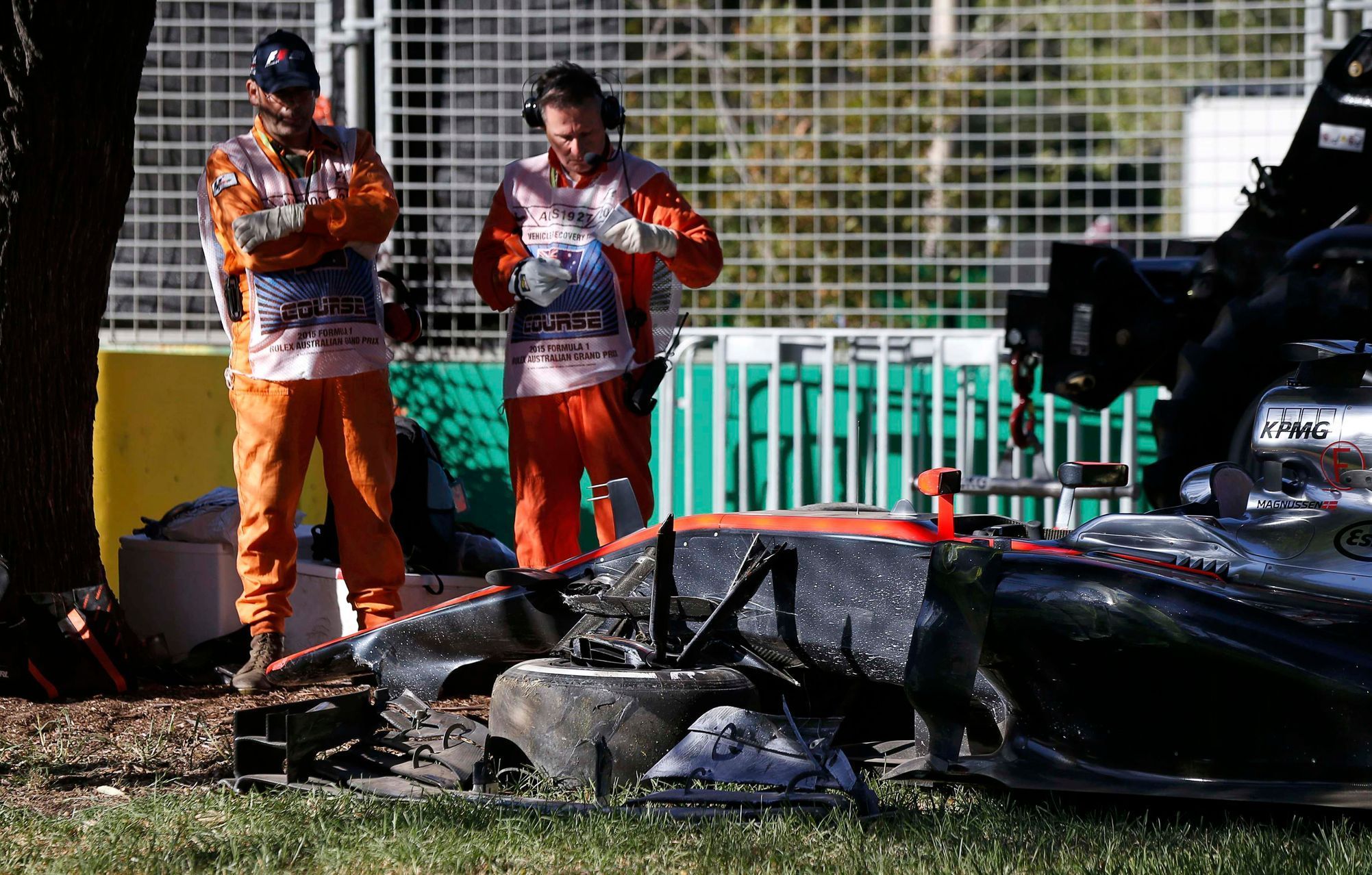 Course officials stand next to the car of McLaren Formula One driver Kevin Magnussen of Denmark after he crashed during the second practice session of the Australian F1 Grand Prix at the Albert Park c