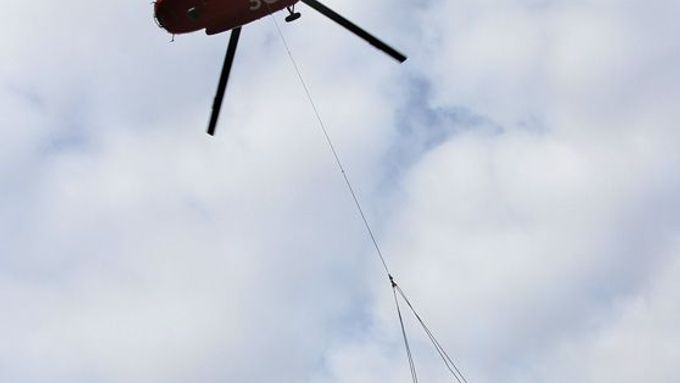 Pod vrtulníkem jsou v podvěsu přepravovány základnové stanice mobilní sítě třetí generace. Před dvěma lety operátor testoval jejich provoz v Nuslích, teď je potřebuje přesunout na střechy ve Vysočanech.