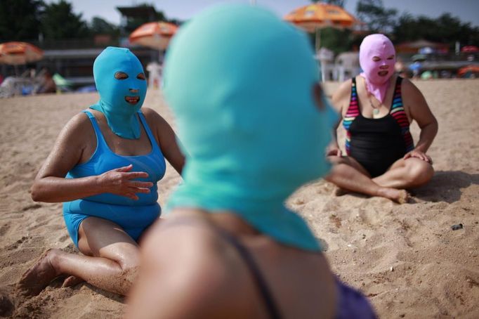 Women, wearing nylon masks, rest on the shore during their visit to a beach in Qingdao, Shandong province July 6, 2012. The mask, which was invented by a woman about seven years ago, is used to block the sun's rays. The mask is under mass production and is on sale at local swimwear stores. REUTERS/Aly Song (CHINA - Tags: SOCIETY TPX IMAGES OF THE DAY ENVIRONMENT TRAVEL) Published: Čec. 6, 2012, 4:03 odp.