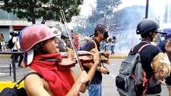 Muž hraje uprostřed zuřící venezuelské demonstrace na housle