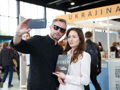 Serhij Žadan se fotí s čtenářkou před ukrajinským stánkem na veletrhu.