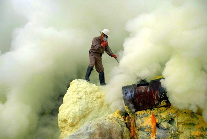 To go with story Indonesia-volcano-mine by Jerome Rivet A picture taken on March 8, 2010 shows Indonesian sulphur miner collecting sulphur surrounded by thick toxic smoke at the Kawah Ijen, or Ijen crater, in Bondowoso in East Java. Indonesian porters at Kawah Ijen, a famous tourist spot in Indonesia's East Java, mine and carry at least 70 kg-worth of sulphur blocks on their shoulders through the suffocating clouds of toxic gases each day receiving just 70,000 to 80,000 rupiah (7 - 8 US dollars) for their labour.