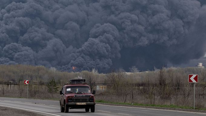 Automobil na silnici z Lysyčansku, v pozadí hoří vybombardovaná ropná rafinérie.