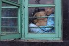 Tibetské děvčátko s medvídkem se dívá z okna svého domu v Dharamsale.