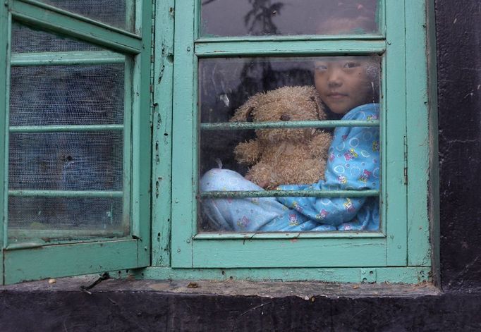 Tibetské děvčátko s medvídkem se dívá z okna svého domu v Dharamsale.