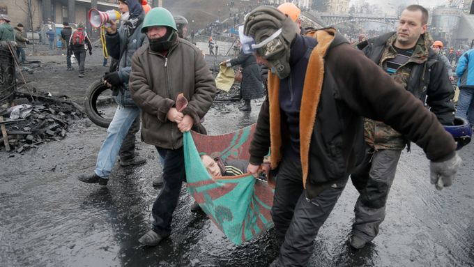 Muži odnášejí zraněného z masakru v centru Kyjeva 20. února 2014.