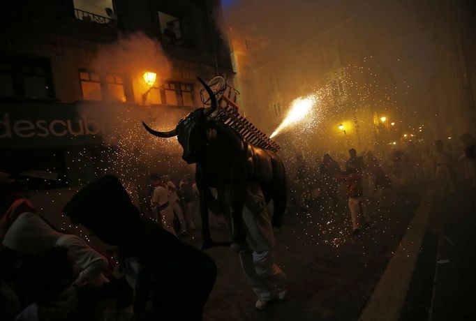 Revellers are showered with sparks from the "Fire Bull", a man carrying a metal structure loaded with fireworks on the fifth day of the San Fermin festival in Pamplona July 10, 2012. Visitors to the nine day festival, depicted in Ernest Hemingway's 1926 novel "The Sun Also Rises", take part in activities including The Running Of The Bulls, an early morning half mile dash from the corral to the bullring alongside six bulls destined to die in the afternoon's corrida. This is followed by processions of giant traditional figures, concerts, firebulls, fireworks, and large doses of eating, drinking, dancing and late nights. REUTERS/Susana Vera (SPAIN - Tags: SOCIETY) Published: Čec. 10, 2012, 9:48 odp.