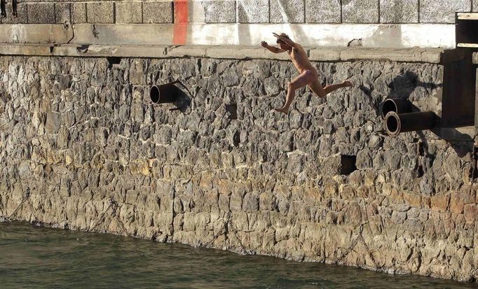 A man jumps from a wall into the Limmat river during sunny summer weather in Zurich August 17, 2012. The Federal Office of Meteorology MeteoSwiss has launched a warning for a heat wave for the weekend until August 22. REUTERS/Arnd Wiegmann (SWITZERLAND - Tags: ENVIRONMENT SOCIETY) Published: Srp. 17, 2012, 6:15 odp.