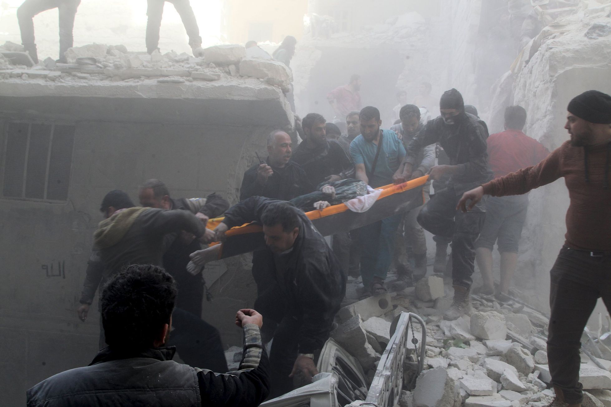 Muži odnášejí ženu ze sutin po bombardování Aleppa.