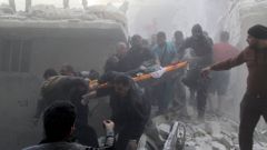 Muži odnášejí ženu ze sutin po bombardování Aleppa.