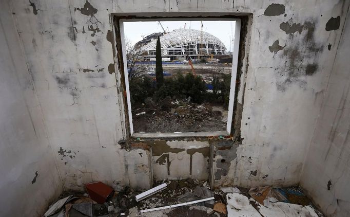 A picture shot through the window of a house that has to be torn down as it is within the perimeters of the Olympic Park shows the Olympic stadium for the Sochi 2014 Winter Olympics at the Olympic Park in Adler, near Sochi February 18, 2013. Although many complexes and venues in the Black Sea resort of Sochi mostly resemble building sites that are still under construction, there is nothing to suggest any concern over readiness. Construction will be completed by August 2013 according to organizers. The Sochi 2014 Winter Olympics opens on February 7, 2014. REUTERS/Kai Pfaffenbach (RUSSIA - Tags: BUSINESS CONSTRUCTION ENVIRONMENT SPORT OLYMPICS) Published: Úno. 18, 2013, 7:52 odp.