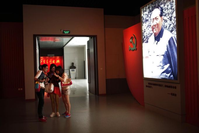 Teenagers look at the screen of a mobile phone as they stand next to a portrait of former Chinese leader Mao Zedong at the Revolution Museum in Jinggangshan, Jiangxi province, in this September 20, 2012 file photo. China's Communist Party has dramatically stepped up its training of the country's roughly 40 million party and government officials in the past decade. With public scrutiny of cadre behaviour growing via social media, the party is likely to call for continued, and deepened, cadre education at the upcoming 18th Party Congress. At the vanguard of this education drive, alongside a Central Party School in Beijing, are three "Executive Leadership Academies" which opened in 2005 for middle-ranking and senior officials in Shanghai, Yan'an and Jinggangshan. The curriculum covers Marxism, Leninism and Mao Zedong Thought, but students may also take finance courses, receive in-depth media training or role-play crisis management scenarios on everything from disease outbreaks to train wrecks. REUTERS/Carlos Barria/Files (CHINA - Tags: POLITICS SOCIETY) Published: Zář. 24, 2012, 1:48 odp.