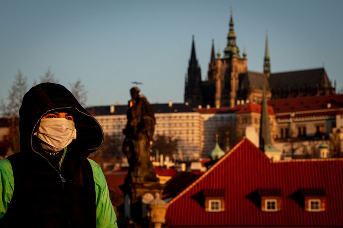 Žena v roušce se prochází po liduprázdném Karlově mostě.