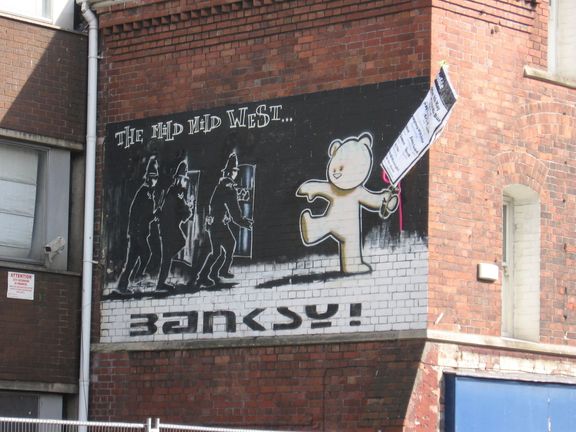 Banksyho graffiti Mild Mild West v Bristolu. Zápalnou lahev překrývá plakát.