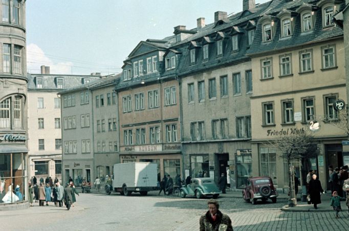 Historická ulice ve Výmaru s měšťanskými domy a obchody, zachycená v 50. letech. V popředí chodci a automobily, v pozadí viditelná cedule hostince "Zum Weisse".