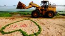 A loader passes by a heart-shape ring of seaweed on the beach in Qingdao in east China's Shandong province Friday July 5, 2013. Thousands of workers are cleaning the beach contaminated by the algae called enteromorpha prolifera each day as the algae blooms in the sea south to the city.