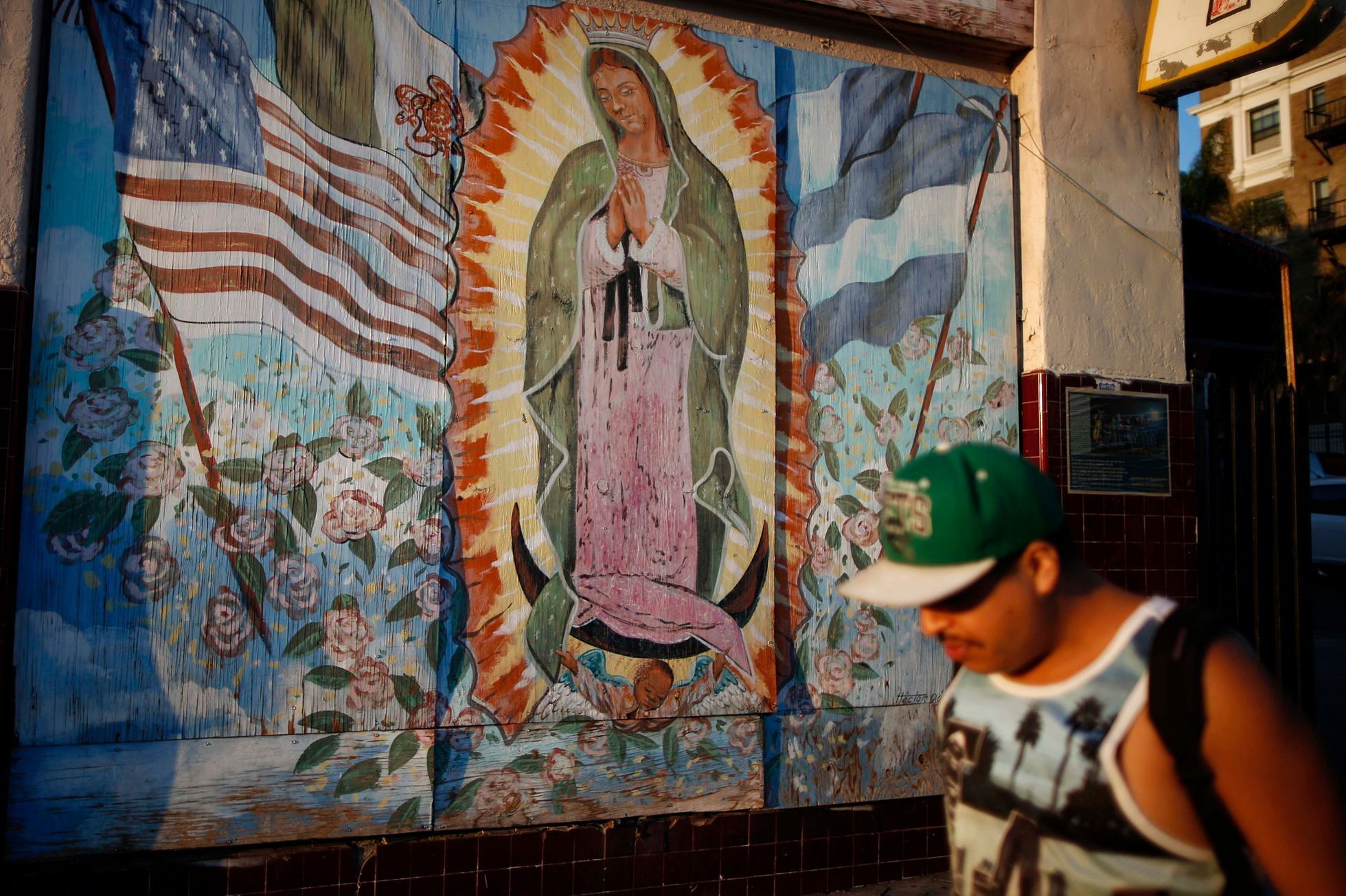 Man walks past a mural showing the Mexican, Salvadoran, Guatemalan and United States flags surrounding the Virgin of Guadalupe in the Westlake area of Los Angeles in California