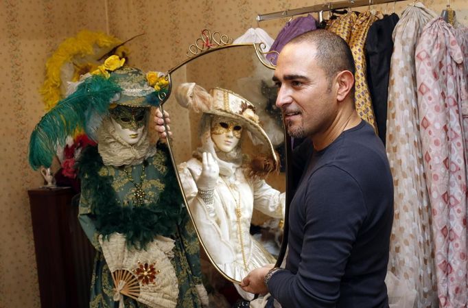 Marco Dilauro looks on as his wife Nadia is reflected in a mirror as she wears one of his creations, an elaborate costume for the Venice Carnival January 25, 2013. Dilauro, 43, is a tax collector by day, but his real passion is making masks and costumes for the carnival. A resident of Como, northern Italy, he chooses fabrics, ribbons, lace and costume jewellery to make the period costumes after doing extensive research, and wears them at Carnival, which ends on the day before Ash Wednesday. Picture taken January 25, 2013. REUTERS/Alessandro Bianchi (ITALY - Tags: SOCIETY) Published: Led. 27, 2013, 11:08 odp.